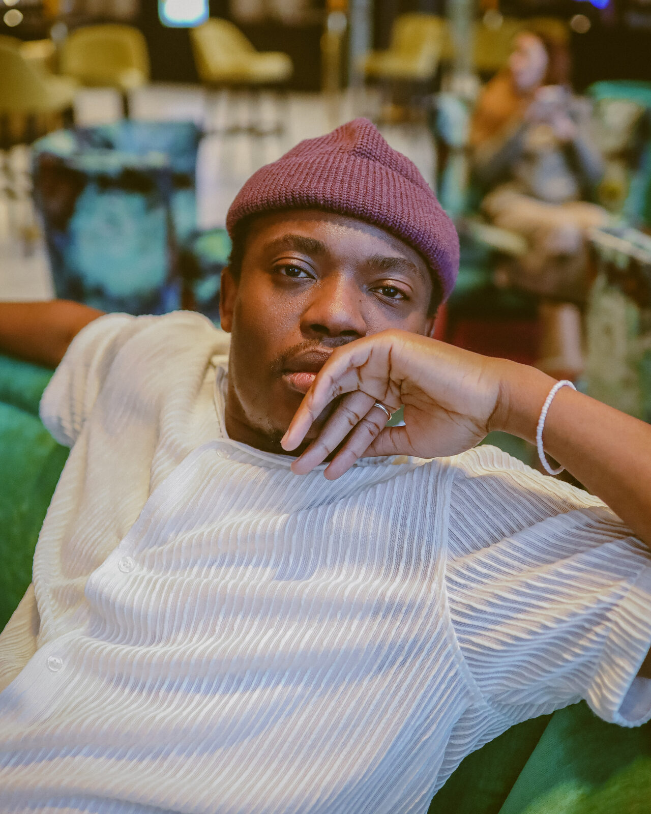 Elvic Kongolo in a pink beanie and white shirt, resting his chin on his hand